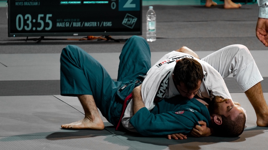 two men competing at a jiu-jitsu tournament, one man is in the side control position