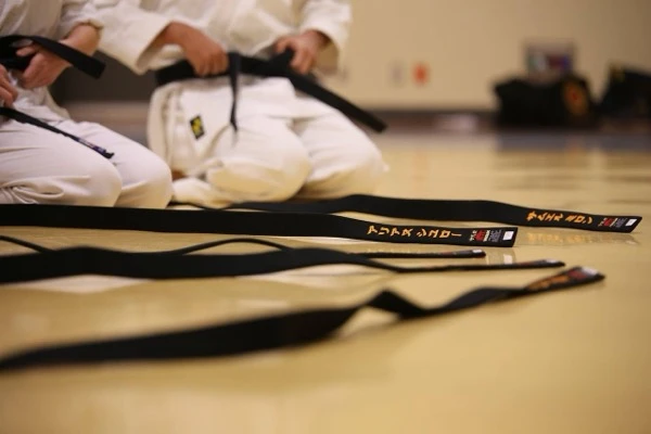 black belts with gold embroidered kanji laid out on dojo floor