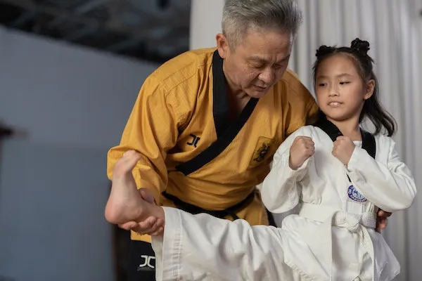 martial arts instructor teaching young taekwondo student proper kicking form